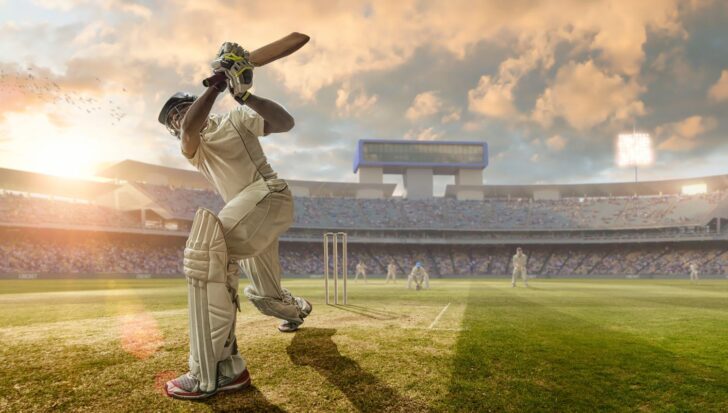 Cricket players on a field with one batsman in the foreground and a stadium full of spectators