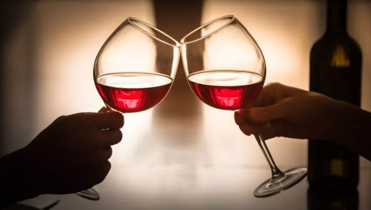 Two hands clinking wine glasses with red wine