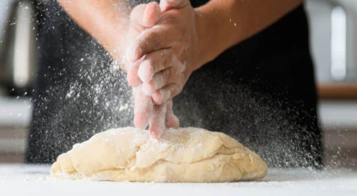 A baker prepares bread and covers their hands with flour