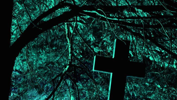 A cross silhouetted against an eerie, illuminated background of tree branches