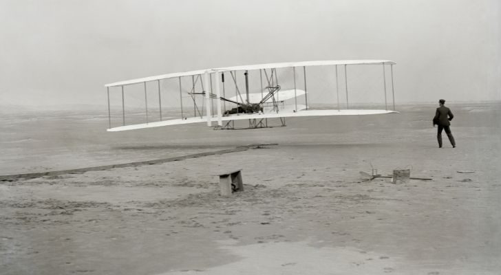 The first flight of the Wright Flyer with Orville piloting and Wilbur running alongside