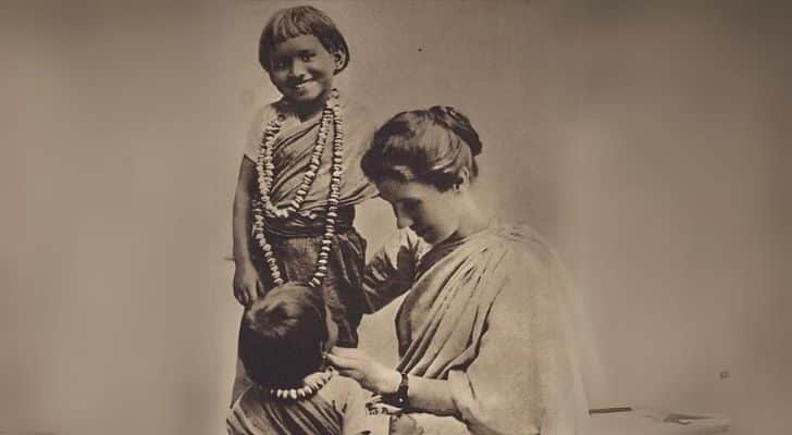 Amy Carmichael adjusting the necklace of a child while another child stands nearby and smiles