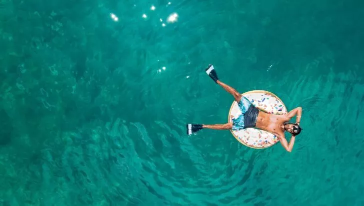 Person floating on an inflatable ring in the middle of a body of water with snorkeling gear and fins