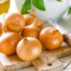 Several brown onions on a wooden cutting board with a knife nearby