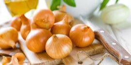 Several brown onions on a wooden cutting board with a knife nearby