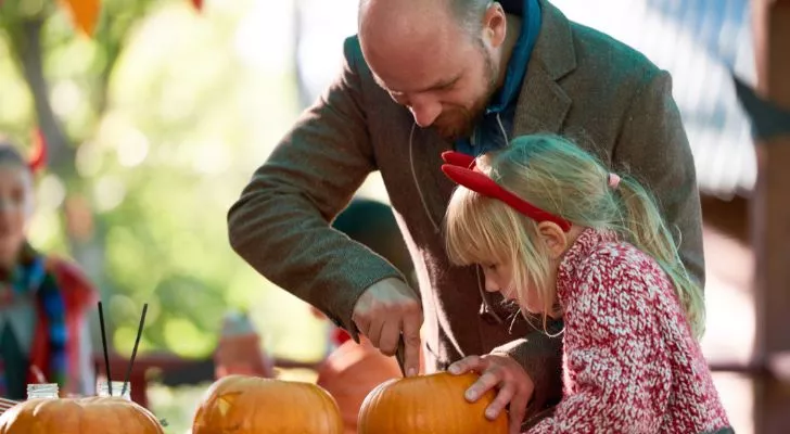 A man helping a young girl carve a pumpkin at a party