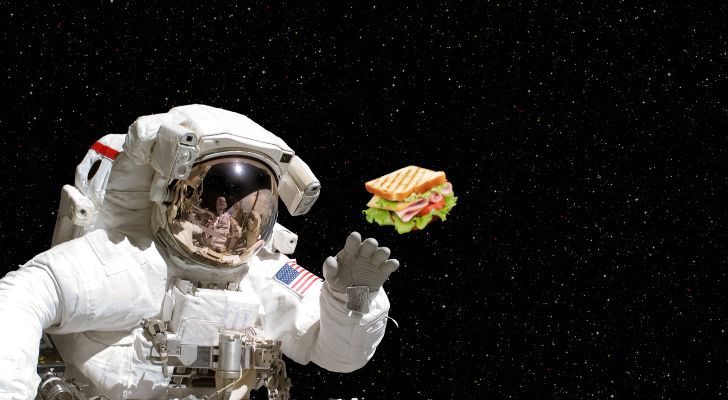 An astronaut with an American flag on their arm against the black backdrop of space, reaching out towards a sandwich