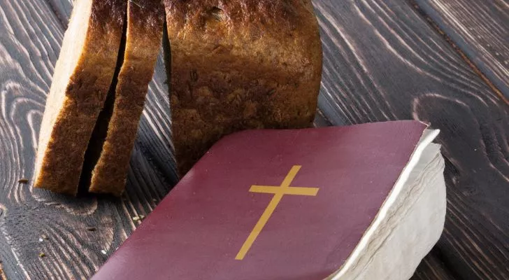 A Bible resting on a table next to a sliced loaf of bread