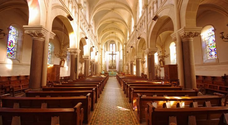 The inside of a well list church with wooden pews and and a large cross at the altar