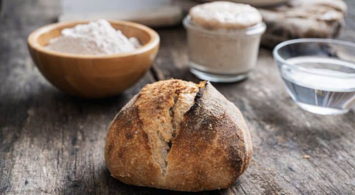 A sourdough loaf sitting on a wooden table next to some flour