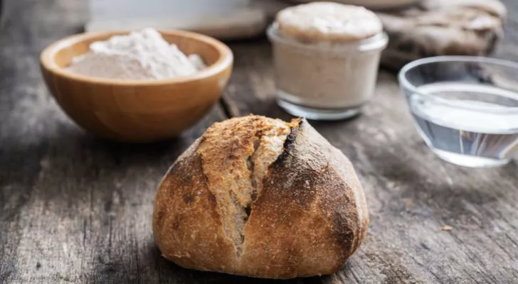 A sourdough loaf sitting on a wooden table next to some flour