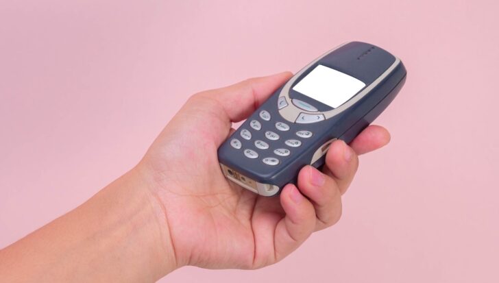 Hand holding an old-style mobile phone against a plain background