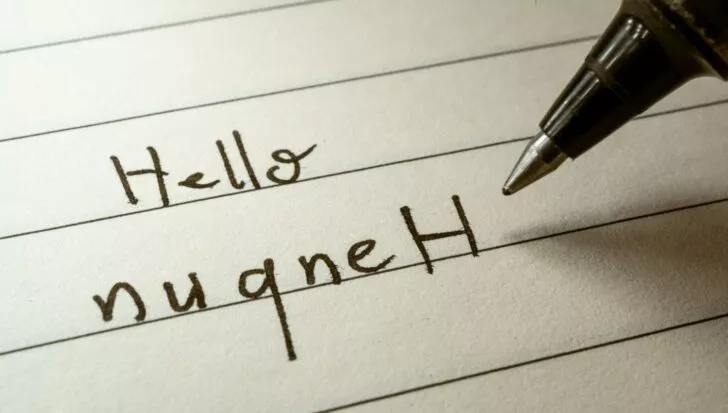 Handwriting of the word 'Hello' in English and its Klingon translation 'nuqneH' on a lined paper with a pen nearby