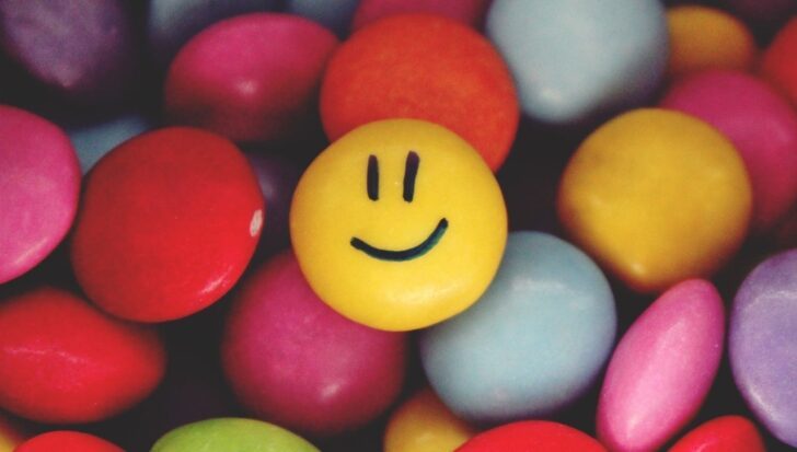 Colorful assorted candies with one yellow candy featuring a smiling face