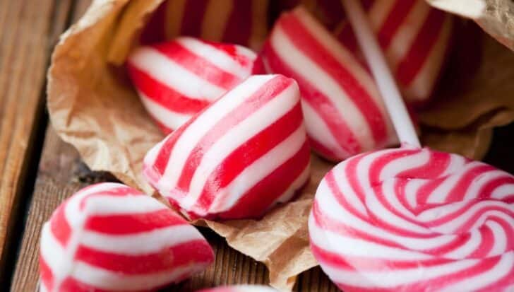 Red and white striped hard candies and a lollipop on a wooden surface