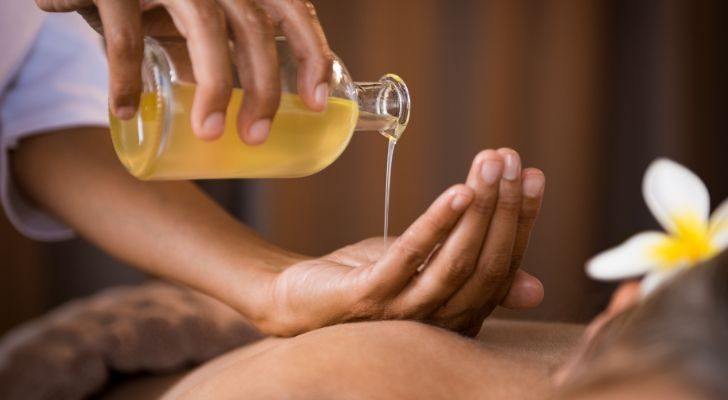 Someone pouring olive oil into their hand to use in a massage