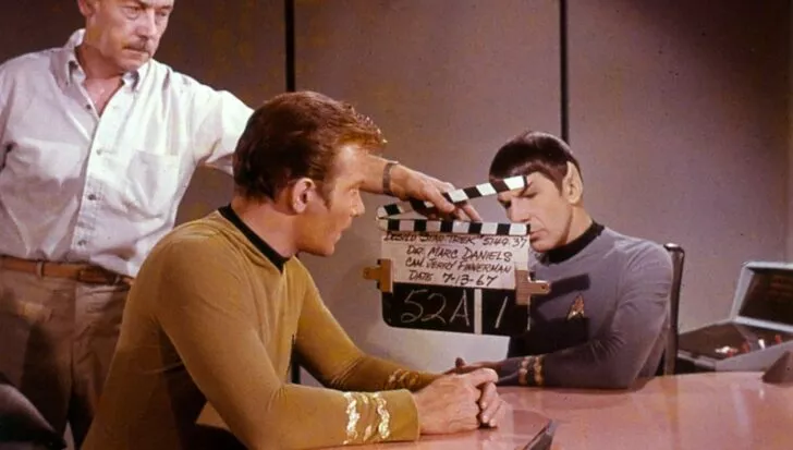 Behind-the-scenes view of Star Trek with three people including a clapperboard, highlighting reused sets from later series