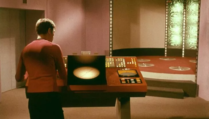 Person operating a control panel in front of a Star Trek transporter platform with illuminated patterns