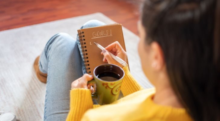 A woman sitting with a notepad and coffee and making a list of goals