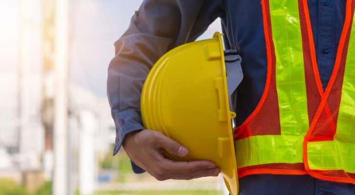 A construction worker wearing work clothes and holding a yellow hard hat