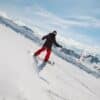 Snowboarder in motion on a snowy mountain slope with clear skies and distant peaks