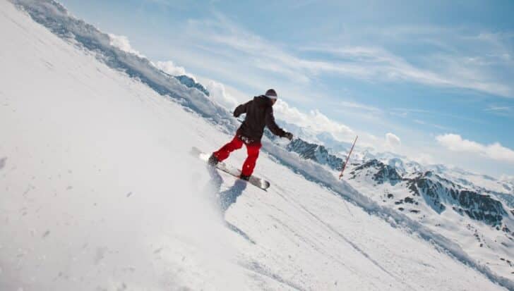 Snowboarder in motion on a snowy mountain slope with clear skies and distant peaks