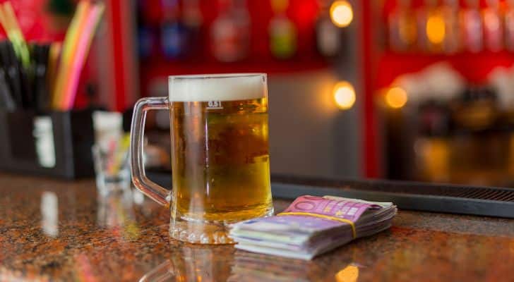 A glass tankard of beer sitting on a bar alongside a stack of money