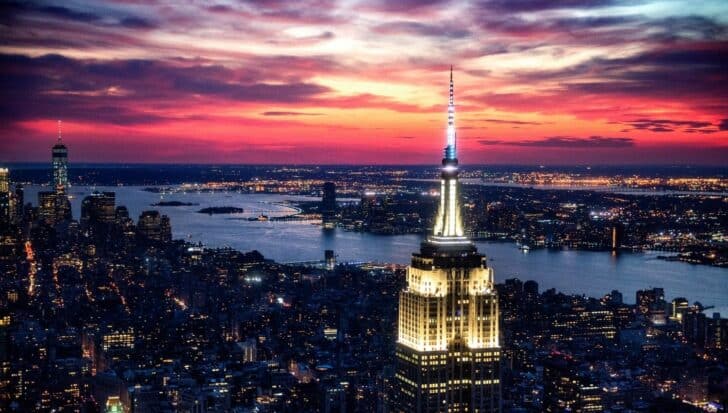 The Empire State Building illuminated at sunset with a view of New York City and the surrounding water bodies