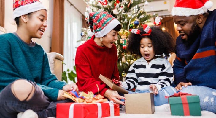 A mom, dad, and their two kids opening presents in front of the Christmas tree