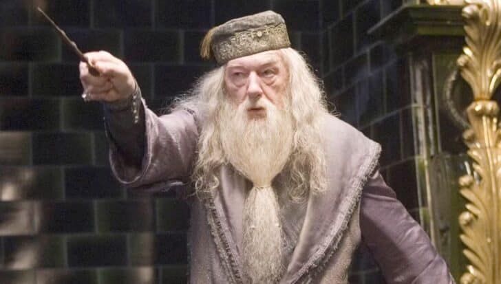 Dumbledore in a robe with a long beard holding a wand in a dimly lit room with dark tiled walls