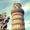 The Leaning Tower of Pisa with a foreground statue of cherubs holding a shield