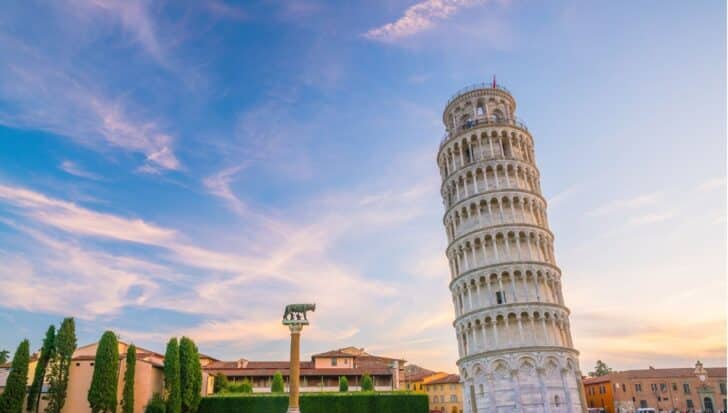 The Leaning Tower of Pisa with a clear blue sky, surrounded by buildings and trees