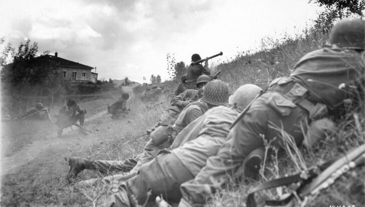 Soldiers lying in a field with rifles during World War II, focusing on a strategic position