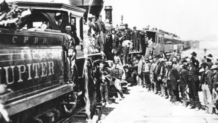 A group of people gathered around locomotives, symbolizing the transportation advancements of the Gilded Generation